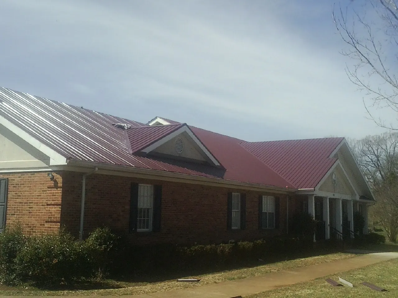 Red metal roof with gabled entries on a long brick building, from a Hail Damage Roof Repair job in Kanaranzi