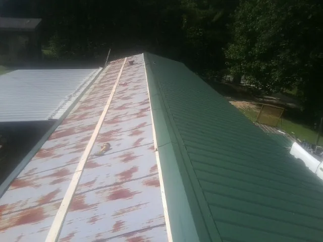 Old rusted panels beside newly installed green metal roofing — Wind Damage Roof Repair by Roofing Brothers in Kanaranzi