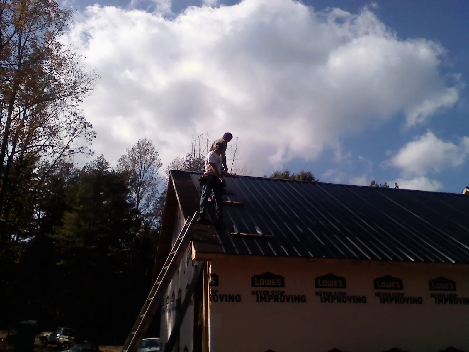 Roofer fastening dark metal panels high against a cloudy sky, from a Roof Inspection job in Kanaranzi