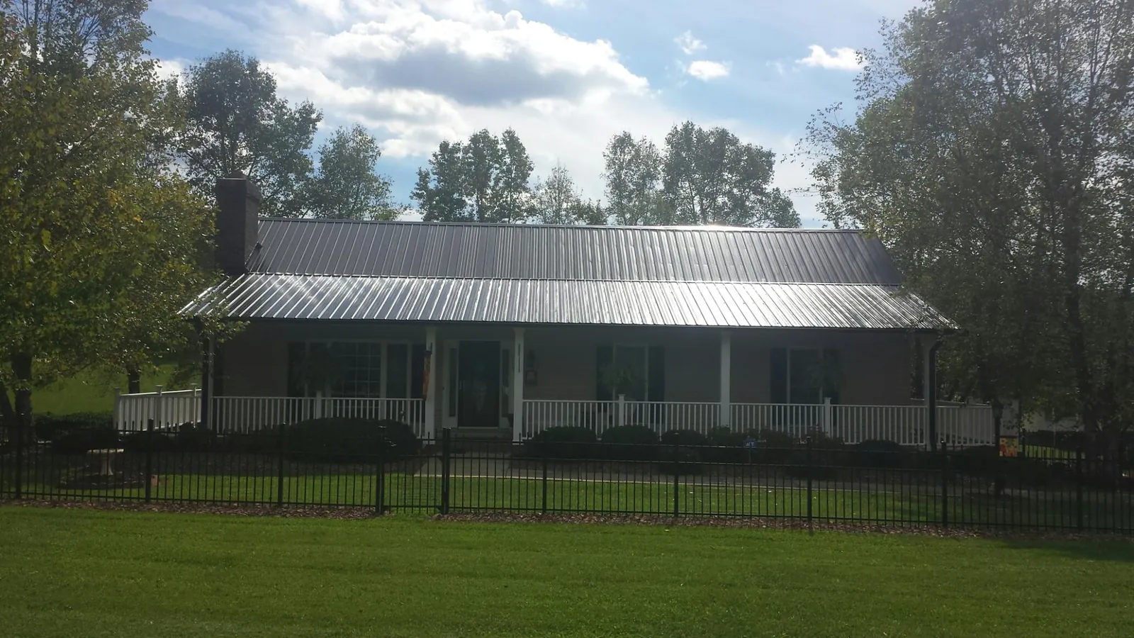 Gray metal roof on a brick ranch with a full width front porch — Gutter Guard Installation work by our crew in Kanaranzi