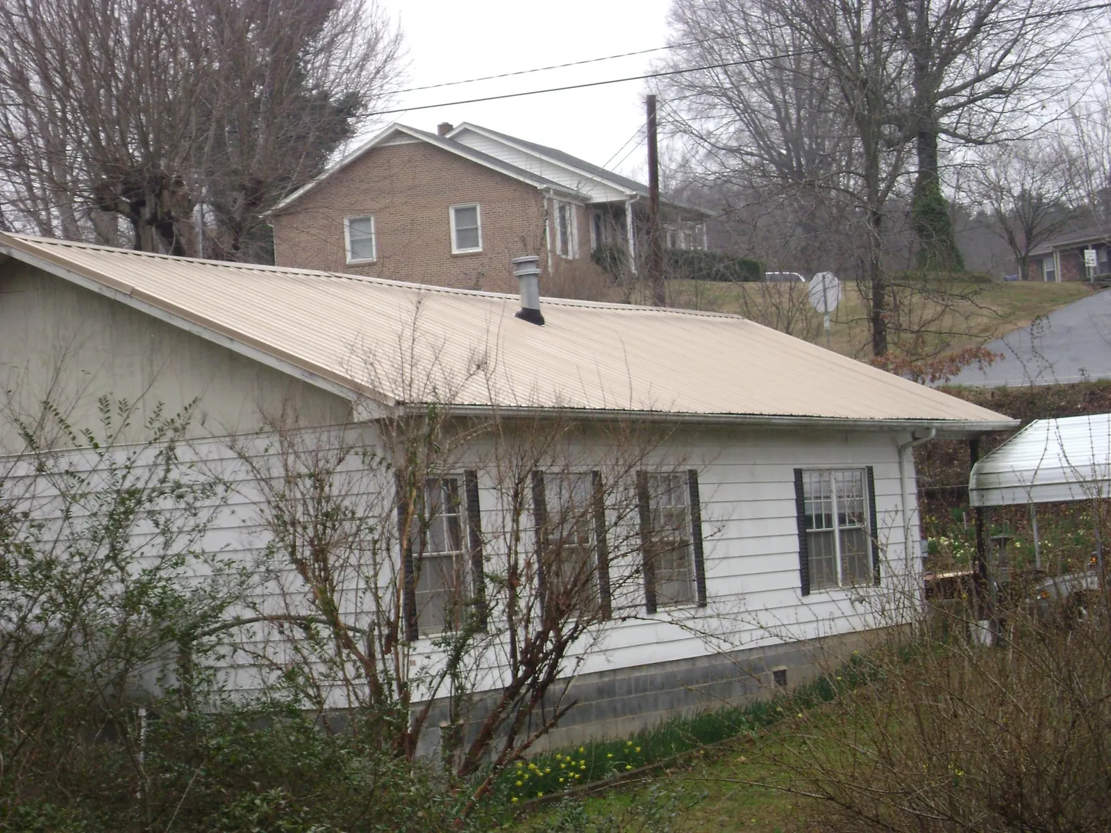 Tan metal roof on a white sided house set into a hillside — Commercial Roofing by Roofing Brothers in Kanaranzi