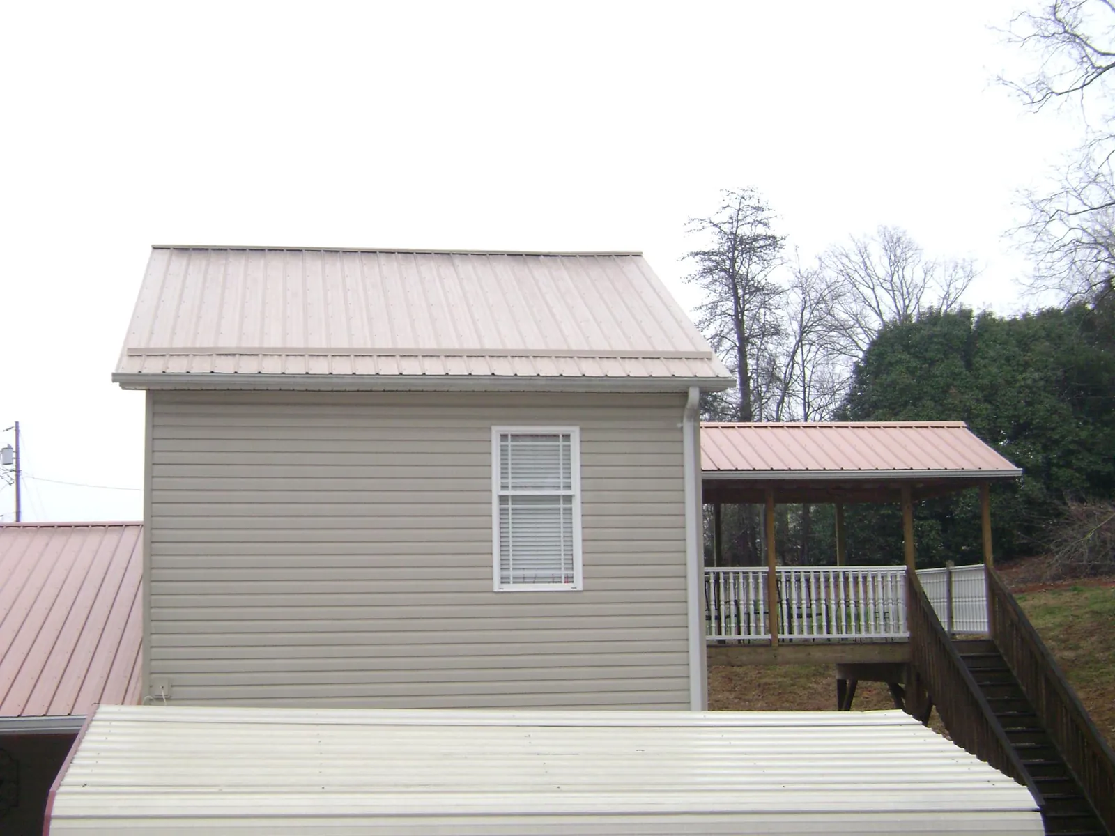 Tan metal roofs on a two story addition and attached porch, from a Roof Replacement job in Kanaranzi